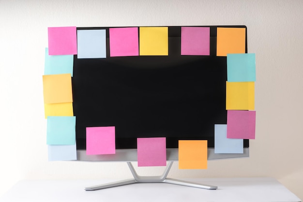 Um monitor de computador exibindo uma variedade de notas adesivas coloridas dispostas em sua tela, colocado sobre uma mesa de madeira.